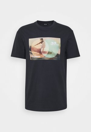 Camiseta de algodón negra con un colorido estampado gráfico de un surfista y el texto "Taxi aéreo y marino. Verano_21 California" en el frente.