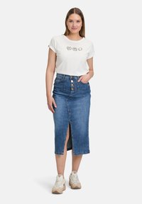 T-shirt blanc avec un texte graphique, associé à une jupe en jean mi-longue avec une fente à l'avant et un bouton de fermeture. Baskets de couleur claire.