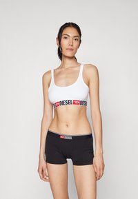 Hvit sports-bh med et svart og rødt "DIESEL" bånd, kombinert med svarte boxershorts med en lignende logo-linning. Enkel design, glatt tekstur.