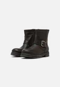 Botas de couro pretas até ao tornozelo com um fecho lateral, uma tira larga com detalhe de fivela e uma sola de borracha texturizada. Design simples e funcional.