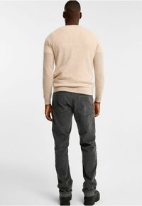 Beige stickad tröja med rund halsringning, ihop med mörkgrå kordflöjlsbyxor med sidofickor och en avslappnad passform. Svarta stövlar fulländar looken.