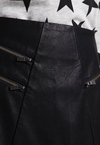 Falda de cuero negra con dos bolsillos con cremallera y una superficie texturizada. El diseño tiene una cintura ajustada y un corte asimétrico.