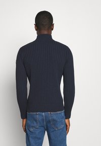 Mörkblå ribbad tröja med hög krage och figursydd design, med strukturerad tyg och långa ärmar, i kombination med blå denimjeans.