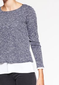 Långärmad tröja i marinblått stickat med en melerad textur, rund halsringning och en kontrasterande vit undertröja synlig vid fållen.