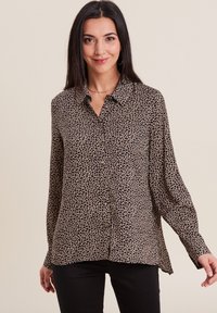 Chemise à boutons en imprimé léopard beige et noir, à manches longues avec poignet, légère texture, tissu doux et design à ourlet arrondi.