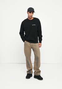 Melna sporta krekls ar ribotām aprocēm un apakšmalu, gaiši brūnas nolietotas džinsas bikses un melni sneakers apavi. Pelēka beisbola cepure noslēdz šo izskatu.