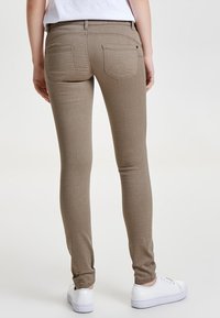 Jeans slim-fit beiges con una textura suave, dos bolsillos traseros y detalles de costura sutiles, combinados con zapatillas blancas.