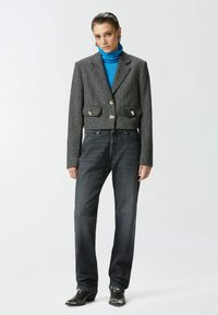 Skraćena siva tvid jakna s dva prednja džepa i kutnim dugmadi, uparena s tamnim trapericama i svijetlom plavom rolkom.