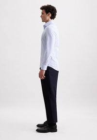 Camicia button-up a righe blu chiaro con maniche lunghe, abbinata a pantaloni scuri navy e scarpe eleganti nere. Design minimalista e linee pulite.