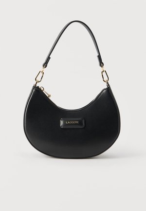 Crna torbica u obliku polumjeseca sa zlatnim detaljima, zatvaračem na vrhu, kratkom naramenicom i pločicom s logotipom "LACOSTE" u sredini sprijeda.