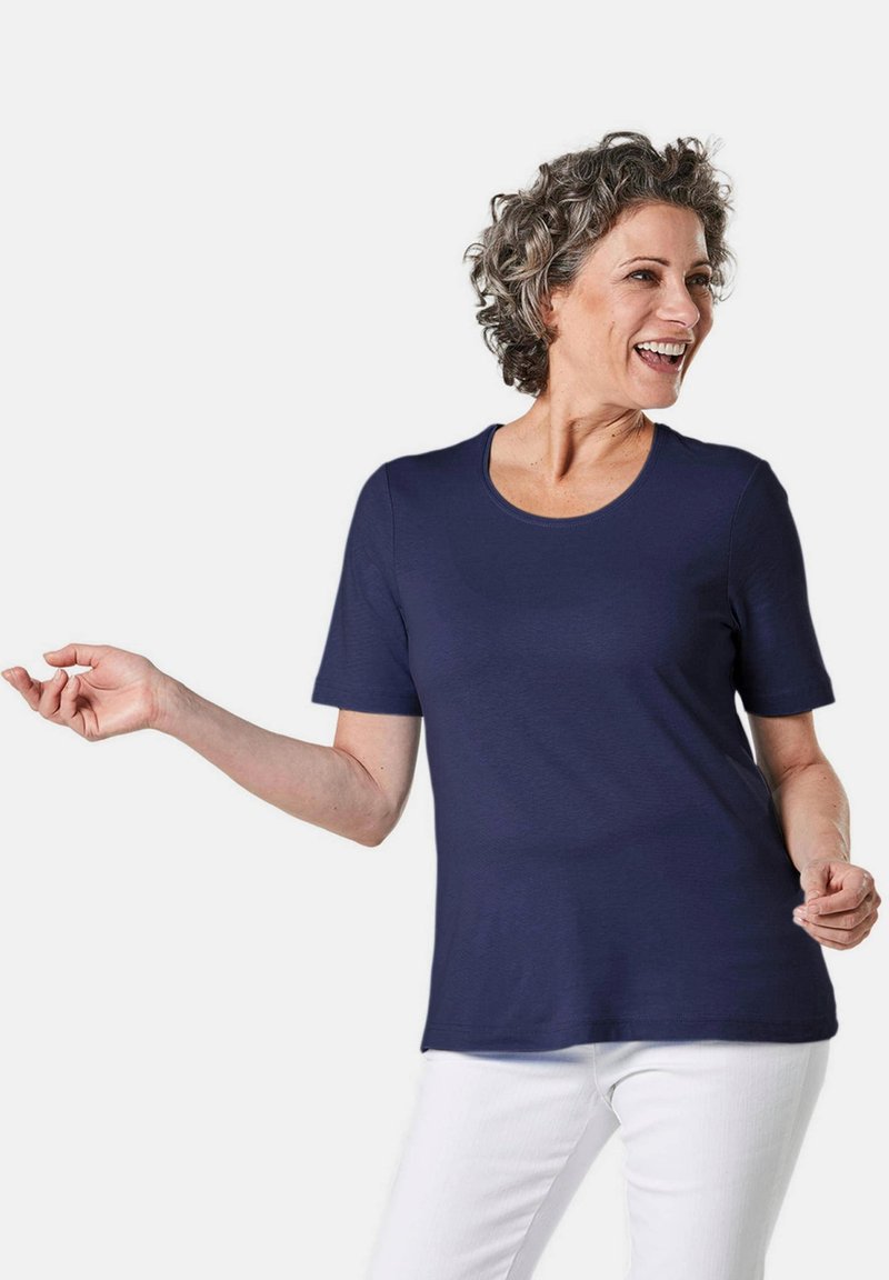 Marineblauw T-shirt met korte mouwen en een ronde halslijn, gemaakt van zachte stof, gedragen met witte broek. Eenvoudig ontwerp, geen zichtbare patronen of accenten.