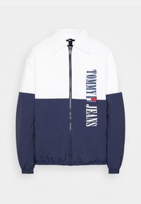 Navy and white zip-up jacket with a collared neck, featuring "TOMMY JEANS" printed on the front and an elastic hem and cuffs.