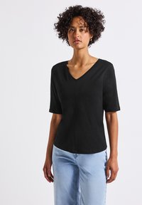 Černé tričko s krátkým rukávem a V výstřihem, volného střihu, vyrobené z lehkého materiálu, ve spojení se světle modrými džíny.