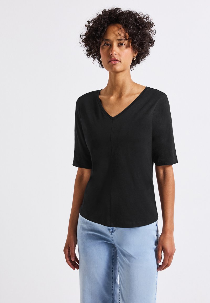 Černé tričko s krátkým rukávem a V výstřihem, volného střihu, vyrobené z lehkého materiálu, ve spojení se světle modrými džíny.
