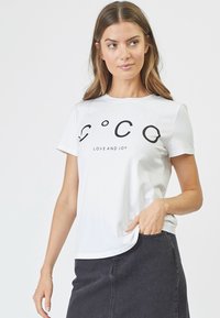 Camiseta blanca de algodón con cuello redondo y mangas cortas, que presenta un fuerte texto negro "C°C° AMOR Y ALEGRÍA" en la parte frontal.