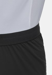 Czarne szorty sportowe z grubym elastycznym pasem. Materiał wydaje się lekki o gładkiej teksturze, odpowiedni do noszenia podczas aktywności.