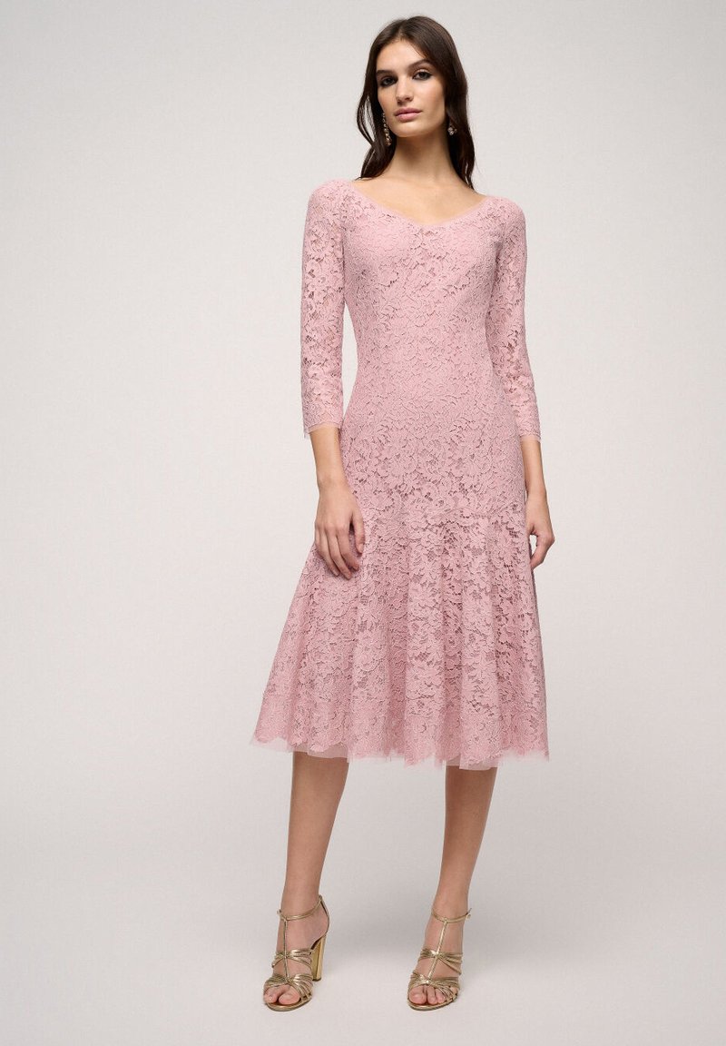 Rochie roz din dantelă, cu decolteu în V, mâneci trei sferturi și tiv evazat. Prezintă modele florale și un material texturat. Asortată cu sandale aurii cu curele.