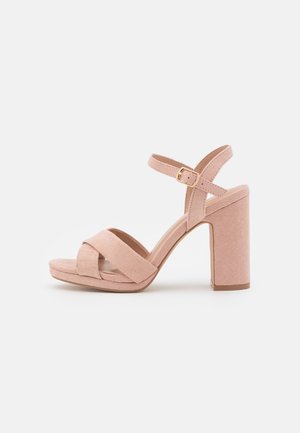 Sandales à talons roses blush avec une texture en daim, présentant un design à bride croisée, une bride de cheville avec une boucle dorée, et un talon carré épais.
