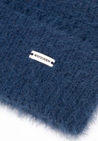 Námořnicky modrý pletený šátek s texturovaným, chlupatým povrchem a stříbrnou štítkem s názvem značky „WITTCHEN“ připevněným.