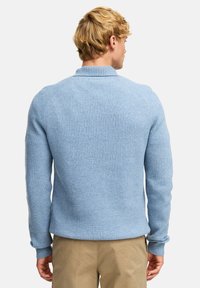 Jasnoniebieski sweter z prążkowanego dzianiny z wysokim kołnierzem, dopasowany w talii i zwężane rękawy. Tekstura wydaje się miękka i gruba.