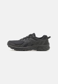 Zapatillas deportivas negras con parte superior de malla, acentos texturizados, diseño de cordones y suela acolchada. Presentan una marca en el lateral y la parte trasera.