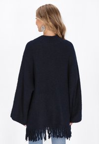 Marineblaues Strick-Poncho mit hohem Kragen, weiten Ärmeln und Fransenrand. Weiche Textur mit lockerer Passform, entworfen für Komfort und Wärme.