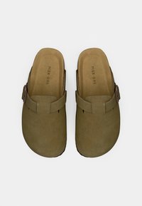 Ein Paar olivgrüne Schlupfschuhe mit verstellbaren Riemen und weichen Einlegesohlen, beschriftet mit "Pier One", auf einem weißen Hintergrund präsentiert.