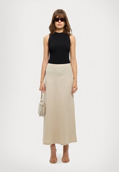 Top senza maniche a coste nere, gonna maxi beige, borsa beige e sandali con tacco color sabbia. La modella indossa occhiali da sole rettangolari scuri.