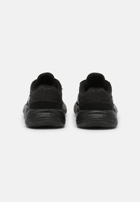 Zapatillas deportivas negras con una parte superior sintética lisa, collar acolchado y suela de goma texturizada. Diseño minimalista sin marcas visibles.