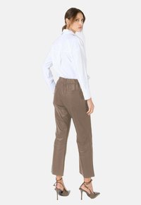 Witte blouse met knopen, gecombineerd met bruine leren, high-waisted, op maat gemaakte broeken en bruine hoge hakken; elegante, gestructureerde stijl.