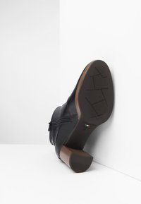 Zwarte leren enkelboot met een ritssluiting, gestructureerde loopzool en een houten-achtige hak. Kenmerkt zich door een slank ontwerp en een gladde afwerking.
