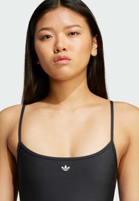 Černé plavky s tenkými ramínky a vysokým střihem. Na středu se nachází malé bílé logo Adidas. Hladká, elastická látka.