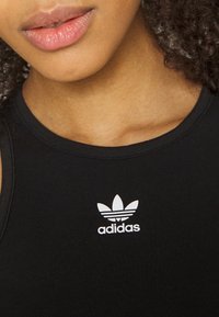 Black athletic tank top with a ribbed texture and a white adidas logo featuring three leaves and horizontal lines near the neckline.
