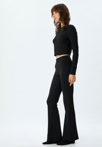 Top corto negro de manga larga con corte ajustado y cuello redondo, combinado con pantalones de campana negros de talle alto, ambos hechos de una tela suave.