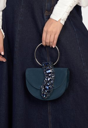Borsa in camoscio verde acqua con manico circolare in argento, caratterizzata da patta decorata con pietre blu scuro e un dettaglio testurizzato.
