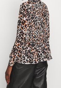 Bluse med leopardprint i let stof, med lange ærmer, plisseret design og rund kant, parret med sorte læderbukser.