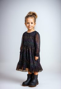 Schwarzes Kleid mit bunten Sprenkeln, langen Ärmeln und einem gewellten Saum; kombiniert mit schwarzen Gummistiefeln. Glatte, glitzernde Stofftextur.