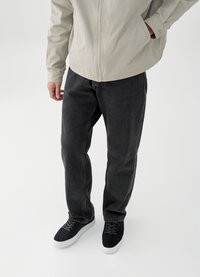 Veste gris clair, jean en denim gris foncé et baskets noires avec semelles blanches. Texture lisse, coupe décontractée et détails matériels minimaux.