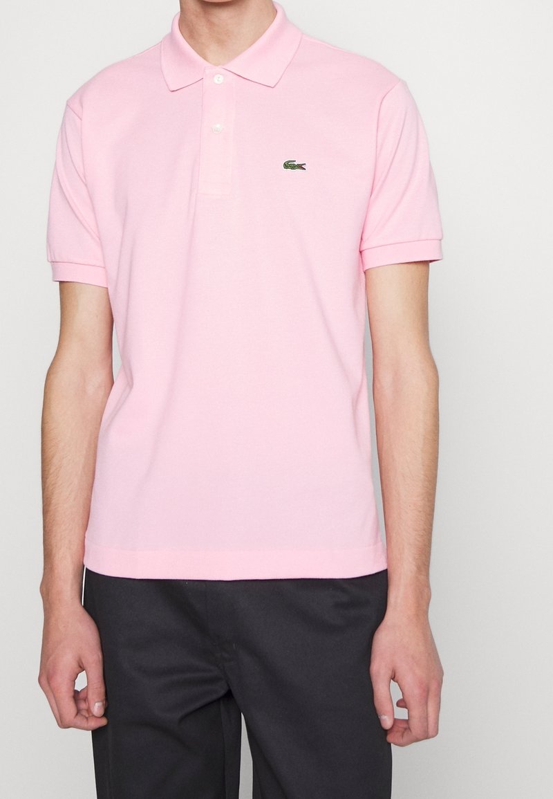 Camisa polo de color rosa claro, hecha de algodón, con cuello extendido, mangas cortas y logo bordado de Lacoste en el lado izquierdo del pecho.