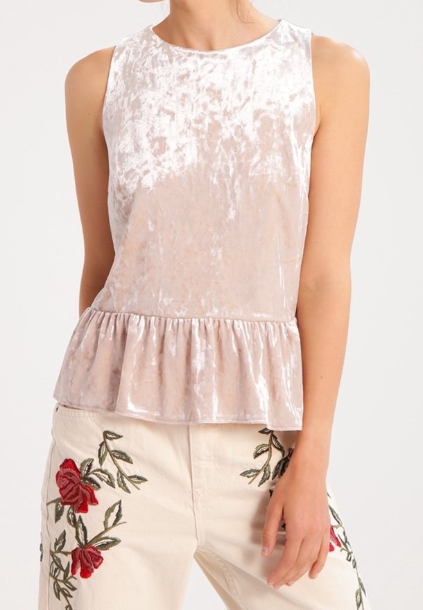 Top senza maniche in velluto rosa chiaro con orlo a peplum. Presenta una texture liscia e un delicato luccichio. Abbinato a pantaloni beige ricamati.