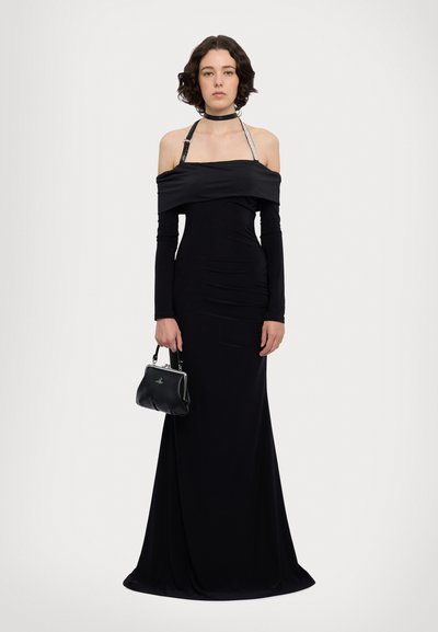 Robe noire épaule dénudée avec manches longues, design froncé et bretelles accent réfléchissantes. Accompagnée d'un petit sac à main noir.