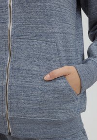 Blå melerad zip-up hoodie med texturerat tyg, som har en främre dragkedja, sidofickor och ribbade ärmslut.
