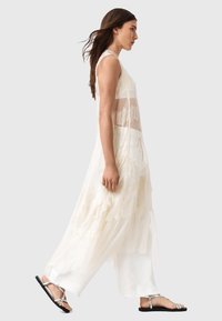 Langes, durchsichtiges weißes Kleid mit Spitzenakzenten und geschichteten Stoffen. Kombiniert mit schwarzen flachen Sandalen, zeichnet sich das Outfit durch ein lockeres, fließendes Design aus.