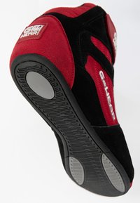 Melni un sarkani sporta apavi ar zamšādas un auduma augšdaļu, gumijas zoli, teksturētu protektoru un logotipa uzlīmi uz papēža. Akcenti kontrastējošās krāsās.