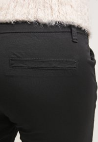 Pantalons noirs en tissu lisse, dotés d'une seule poche arrière avec un rabat et des coutures subtiles. La texture semble douce et propre.