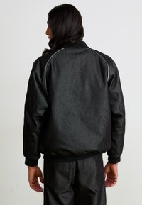 Chaqueta bomber negra con un acabado texturizado, puños y cinturilla elásticos, y sutiles detalles de costura en gris. Combinada con pantalones a juego.