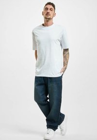 Camiseta blanca de algodón, corte relajado, combinada con pantalones vaqueros oscuros de denim sueltos. Zapatillas blancas completan el look. Diseño simple y casual.