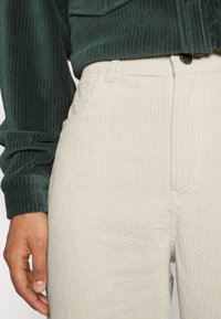 Groene corduroy langemouwen shirt gecombineerd met beige geribde corduroy broek, met een knoopsluiting en gestikte accenten.