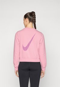Sweatshirt rose avec une texture côtelée, présentant un grand logo Nike à rayures violettes au dos. Design court et manches longues.