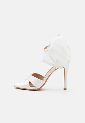 White high-heeled sandal features satin straps and a sheer fabric accent at the back. Smooth texture and open-toe design. Elegant silhouette.